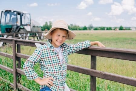 Smiling young boy wearing hat leaning on fence in the farm