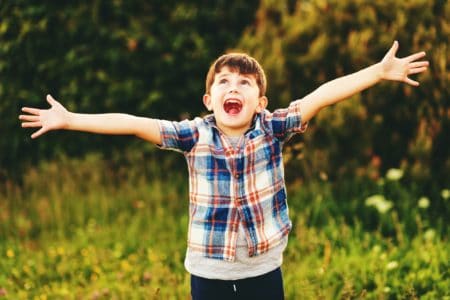 Happy kid boy having fun outdoors wearing blue plaid shirt, arms wide open