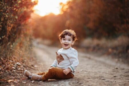 Happy little curly child sitting on the ground in autumn forest