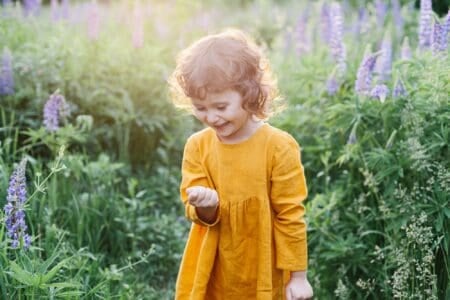 Adorable little girl wearing mustard linen dress with ladybug among lupine flowers