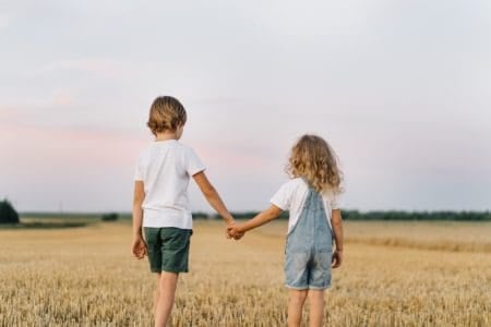 Brother and sister in a mowed field of wheat while holding hands