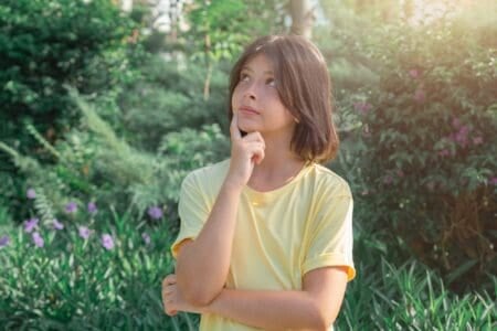 Pretty young girl putting finger to her cheeks while looking up in green park