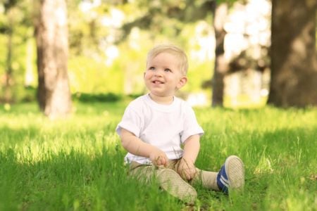 Cute toddler boy with dandelion in green park on sunny day