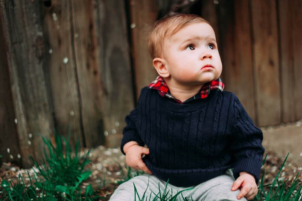 Baby boy in black sweater sitting on the grass