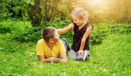 Older brother looking at her little sister while lying on the grass at the park