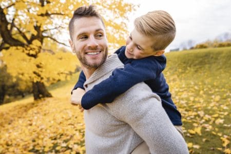 British father giving a piggyback ride to his little son in the autumn park