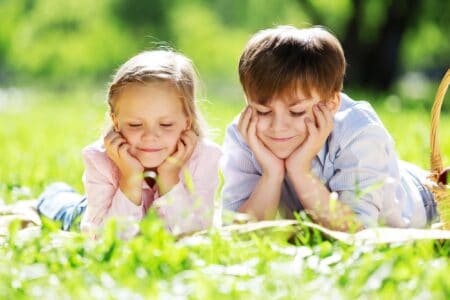 A boy and a girl reading a book while lying on the grass