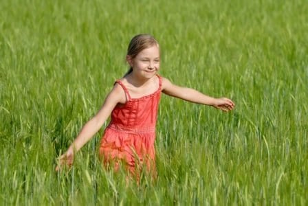 Adorable young girl in red dress running on green field