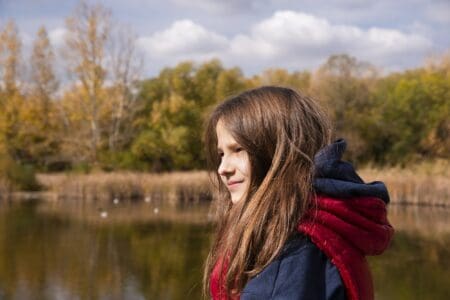 Pretty girl with long hair wearing jacket near the lake shore during autumn