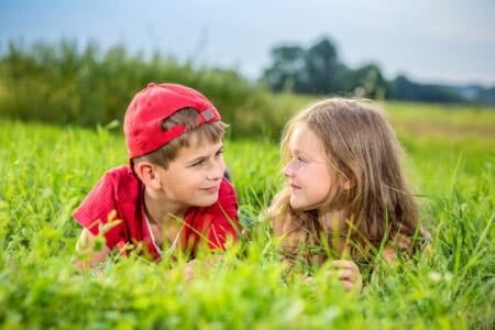 Happy boy and girl looking at each other lying down on green grass on sunny day