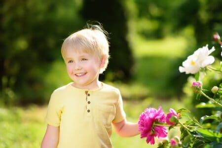 Happy little boy standing near peonies