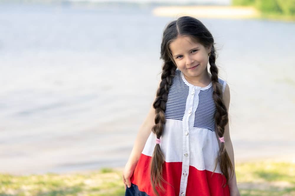 Smiling adorable little girl with long braided hair near the lake