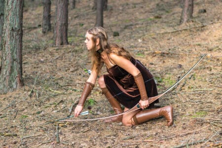 Young lady with elf costume and holding long bow in the wild forest