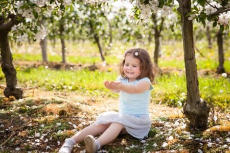 Cute little girl playing with falling cherry petals in the park