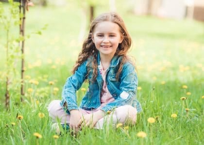 Cheerful cute girl sitting on green field with flowers