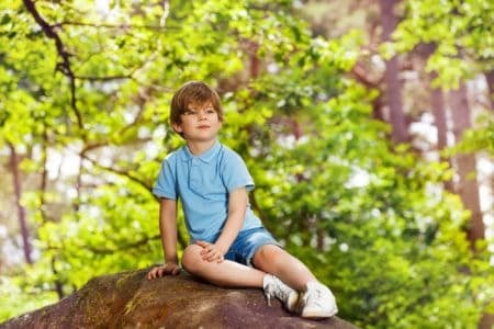 Little boy sitting on stone in the forest