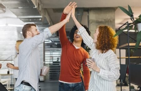 Group of three happy people doing high five at their workplace