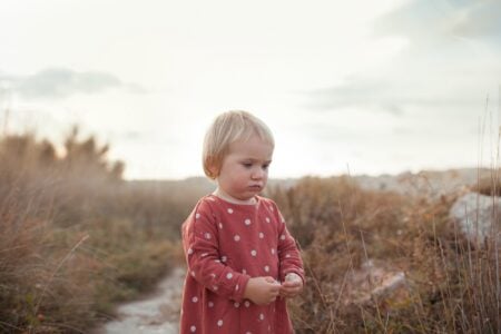 Little pretty girl in red dress walking in the middle of autumn meadow