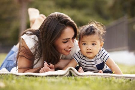 A Hispanic mother lying on a blanket in the park with her baby girl