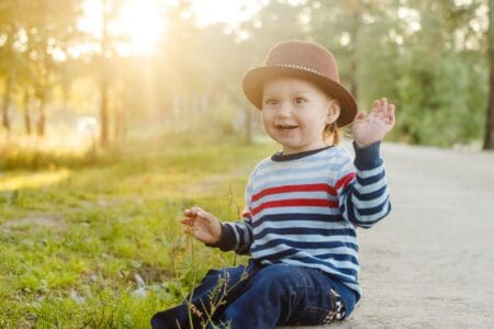 Cute boy in brown hat sitting on ground near the lawn