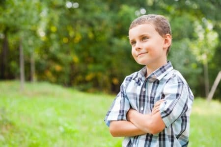 Cute boy standing outdoor in grass field on a sunny day