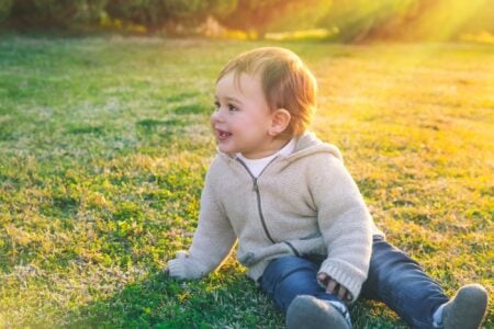 Cute sweet little boy sitting on fresh green grass field in sunny day