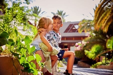 Two young children sitting in a wooden house at the playground.