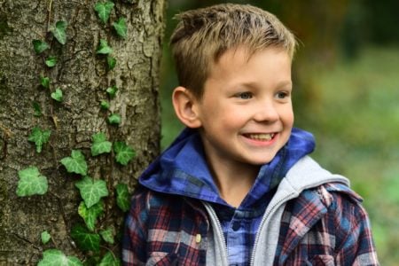 Happy little boy playing near trees in the park