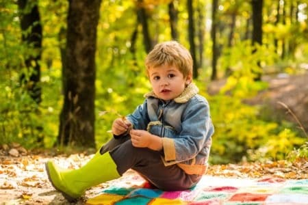 Cute little boy sitting on plaid mat in autumn forest