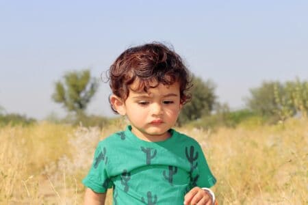 Curly haired cute boy in green tshirt standing outdoor on sunny day