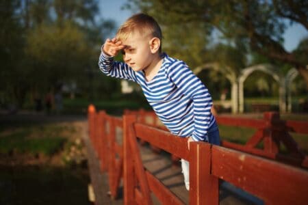 Cute boy looking something from afar while standing near the fence at the park