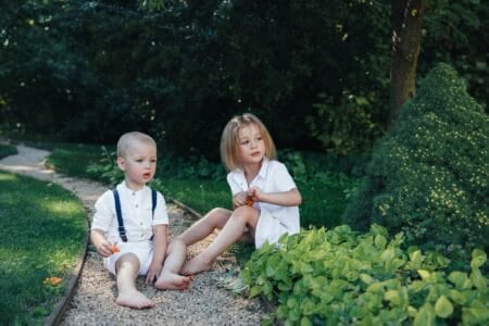 Brother and sister in white clothes sitting in the meadow