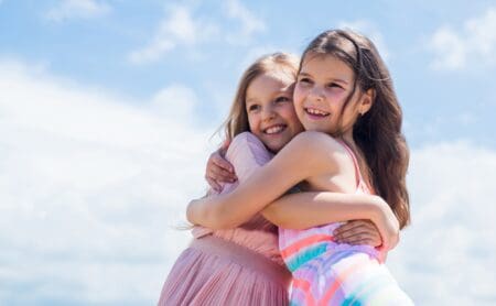 Two beautiful sisters hugging each other against sky background