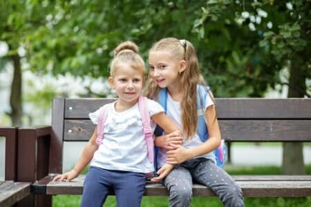 Girls with backpacks sitting on a bench at the park