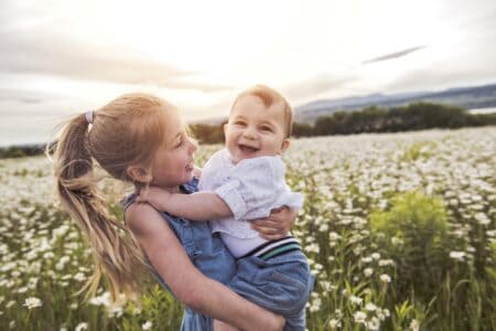 Happy young girl at the field carrying her baby brother