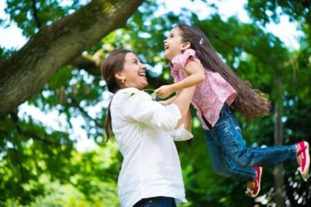 Latin mother lifting her daughter up in the air at the park