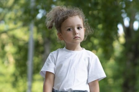 Beautiful little girl in white t-shirt looking at camera with serious face