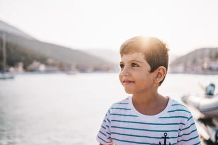 Adorable little boy smiling at sunset with sea and mountain in the background