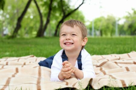 Little boy in denim overalls lying on the picnic blanket in the park