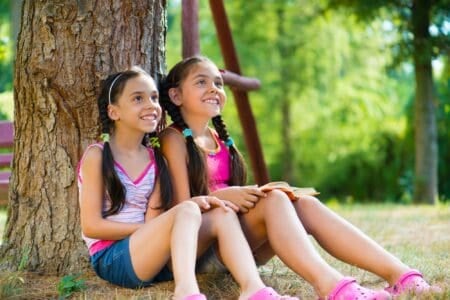 Mexican sisters sitting under the tree both smiling and looking up