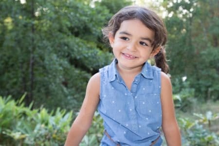 Adorable little girl in blue dress smiling happily with nature in the background