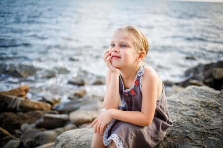 Happy blonde girl sitting on a rock on the seashore