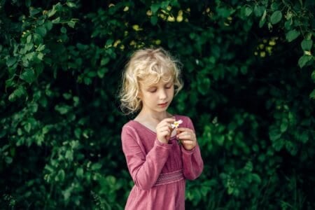 Beautiful blonde girl in pink dress tearing chamomile petals