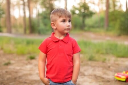 Little young boy in red shirt with hands in his pocket standing at the park