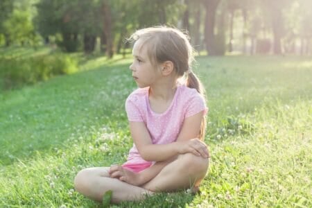 Little girl wearing pink t-shirt sitting on the grass at the park