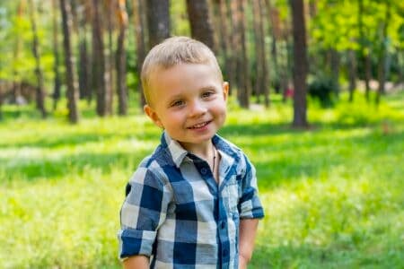 Smiling little boy standing in the park on sunny summer day