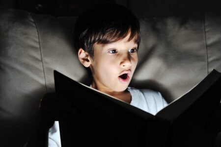 Little boy reading a book in the dark room