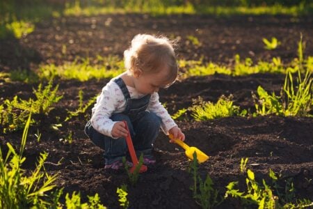 Little boy playing with toy shovels in the garden