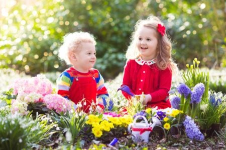 Little boy and girl dressed in red water flowers in the garden