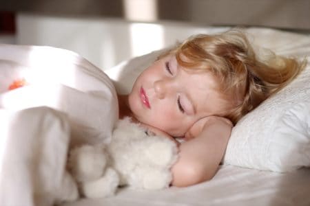 Sweet little child sleeping in bed with a stuffed toy